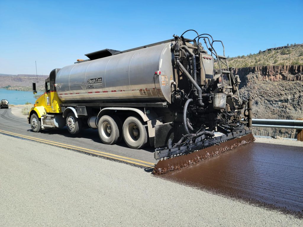 Chip seal truck applying asphalt on a highway near lake in Madras, Oregon.