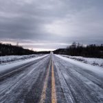 A lonely snow-covered road under a cloudy sky in winter.