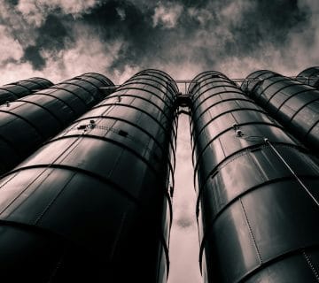Low angle view of industrial silos with a dramatic cloudy sky in the background, emphasizing modern industry.